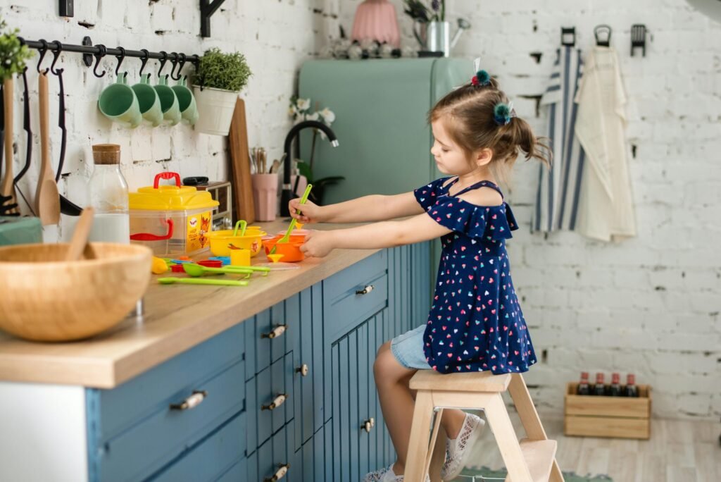 A young girl plays with plastic kitchen toys on a wooden counter, creating a playful atmosphere.