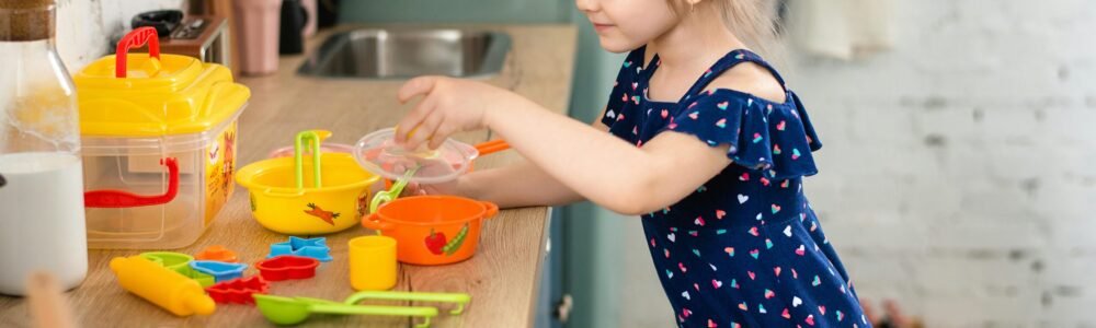 Young girl engaged in imaginative play with kitchen toys on a countertop.
